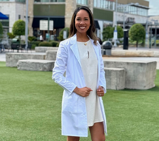 Pearland dentist Doctor Kyrslyne Thomas smiling in a white lab coat over an off white dress