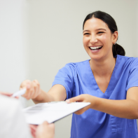 Smiling dental team member handing a clipboard and pen to a patient